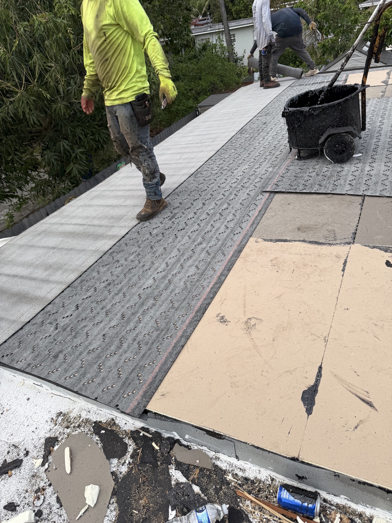 Workers laying base sheet on a flat roof with hot-mop cart