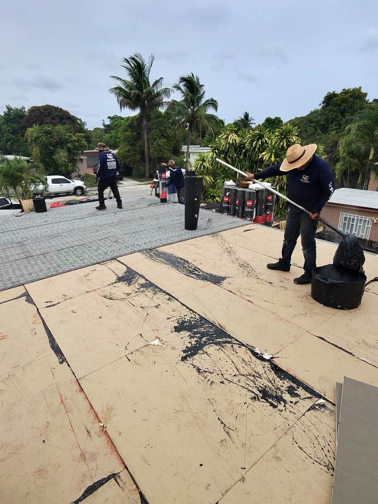 Worker spreading hot mop on insulation boards, RE Builders crew