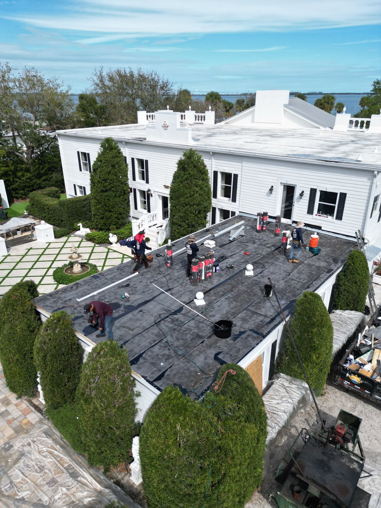 Aerial of crew installing cap sheet on a flat roof of a white house
