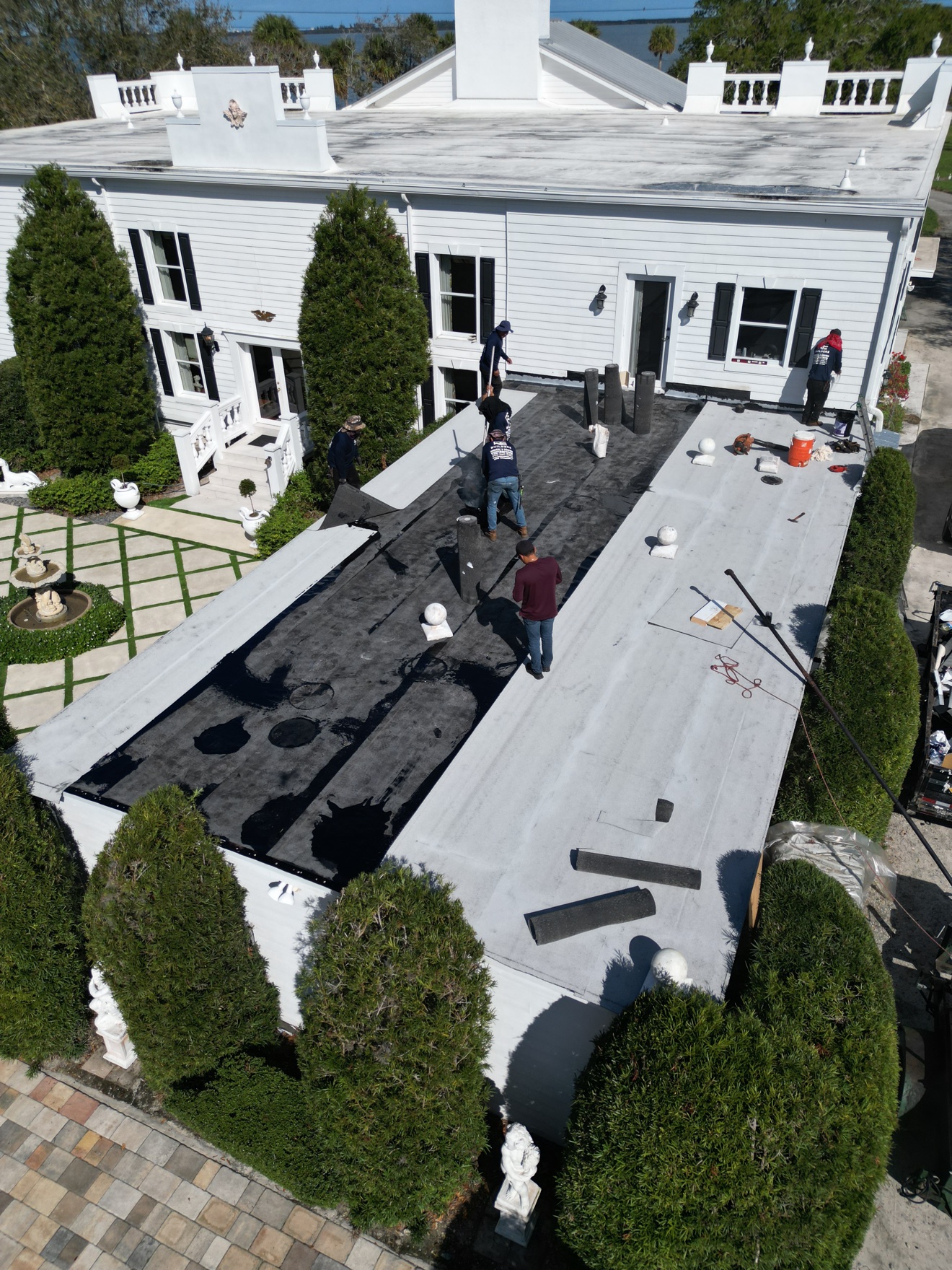 Aerial of crew on a flat roof with black membrane and white house behind