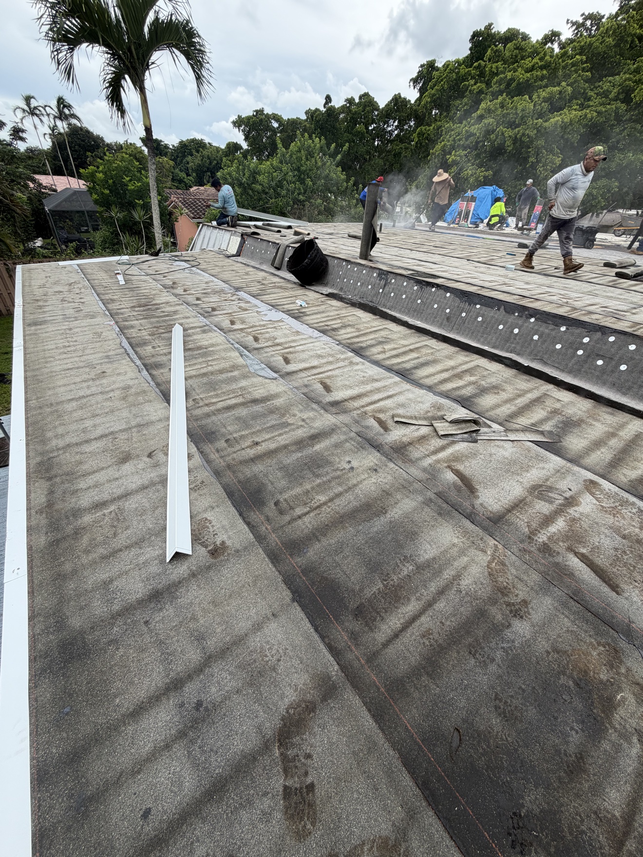 Crew installing cap sheet on a flat roof with white flashing