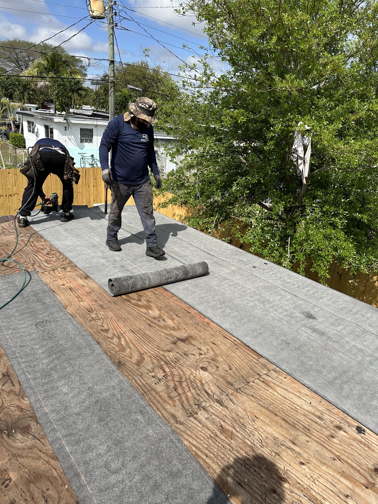 Workers laying base sheet on a plywood deck