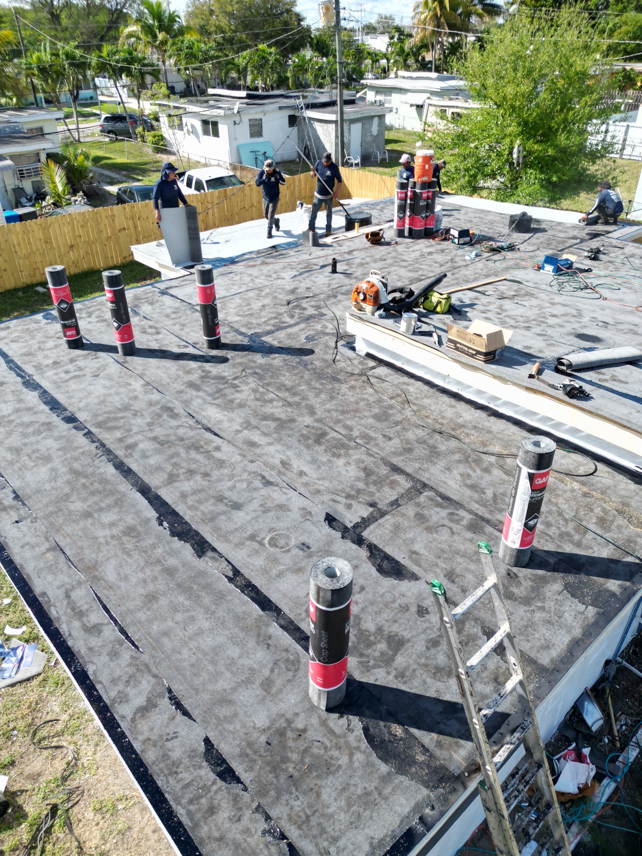 Crew installing modified bitumen rolls on a flat roof, GAF rolls staged