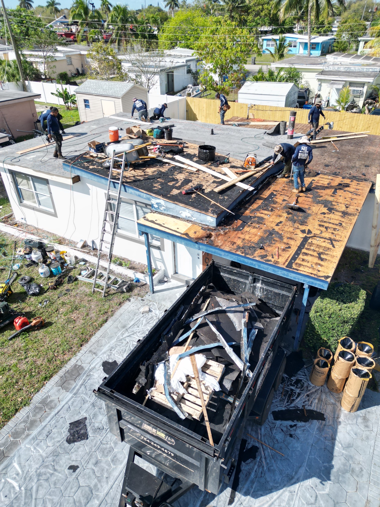 Crew doing tear-off on a flat roof with dump trailer