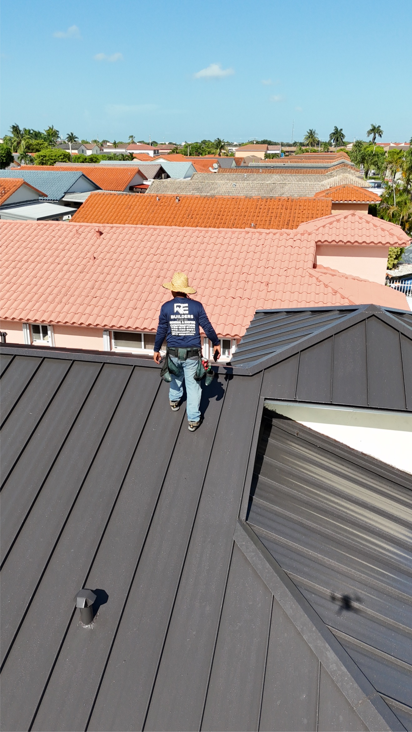 RE Builders worker on a metal ridge with tile roofs behind