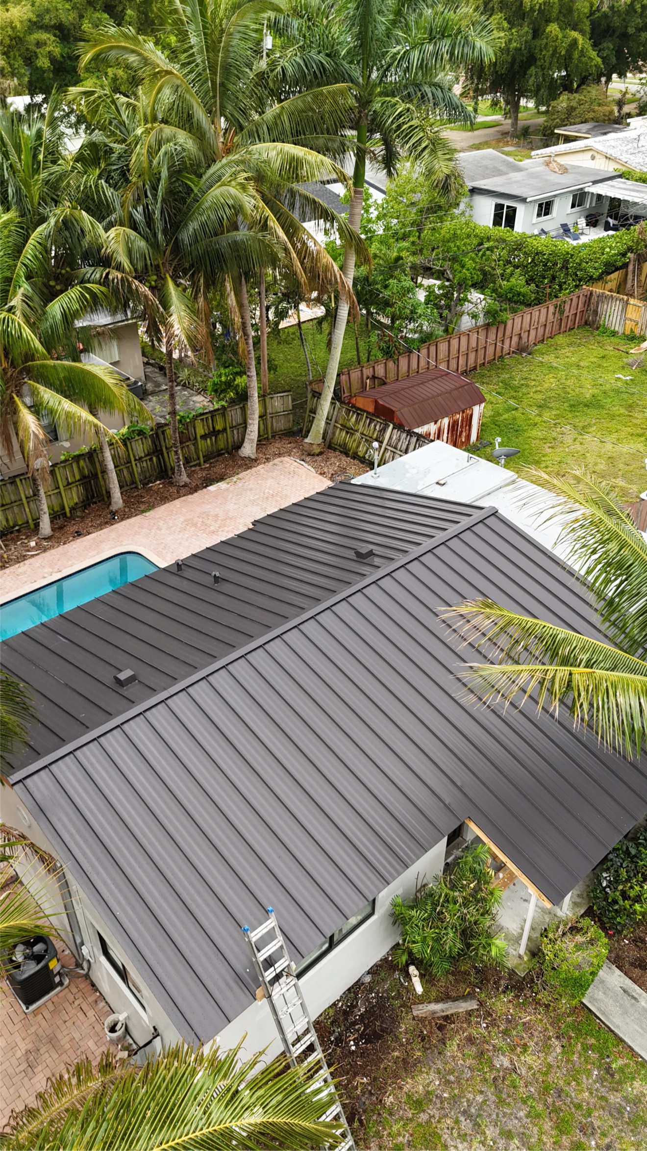 Aerial view of completed dark standing seam metal roof with pool