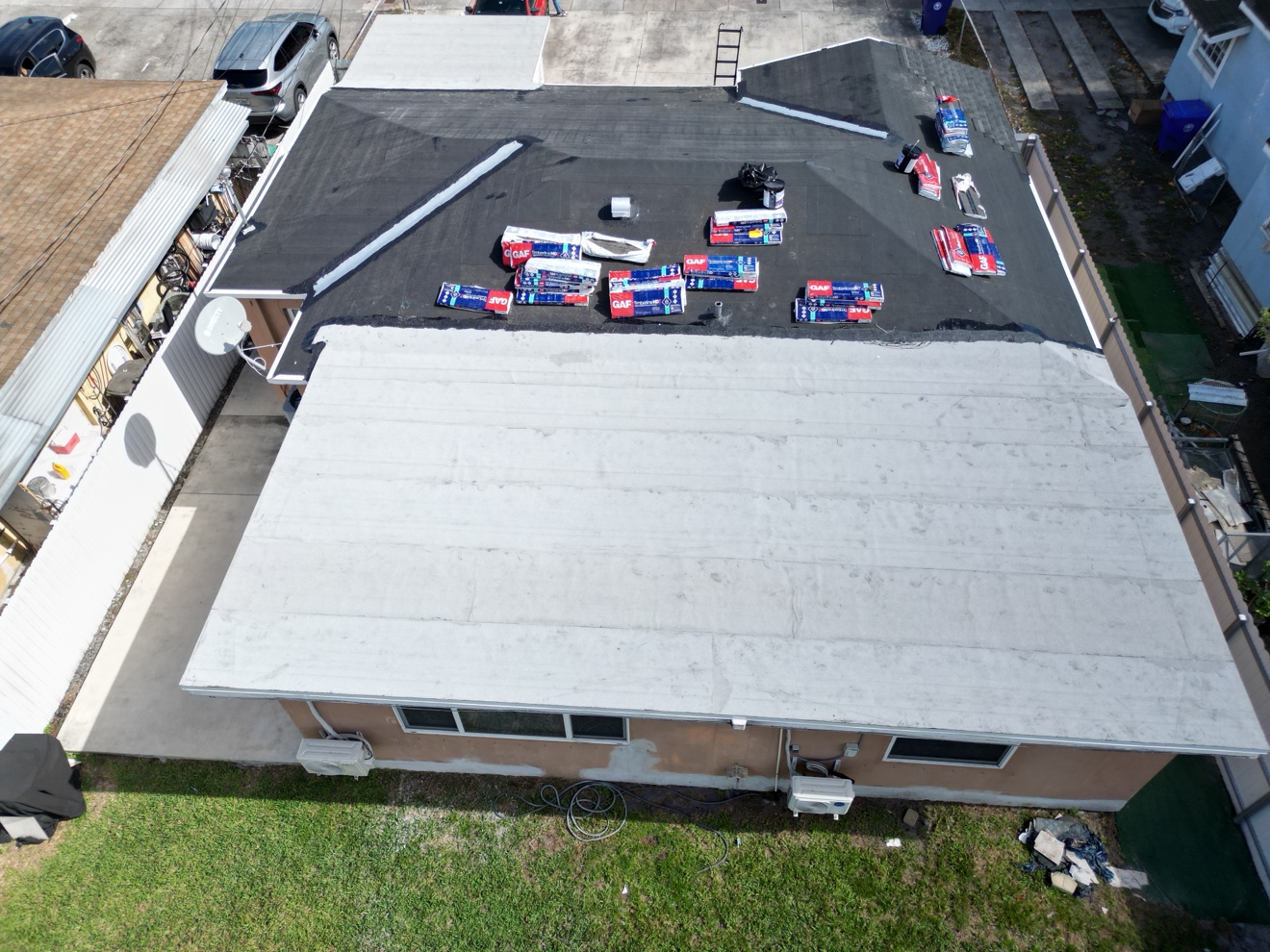 Aerial of a shingle roof job with flat section and GAF bundles staged