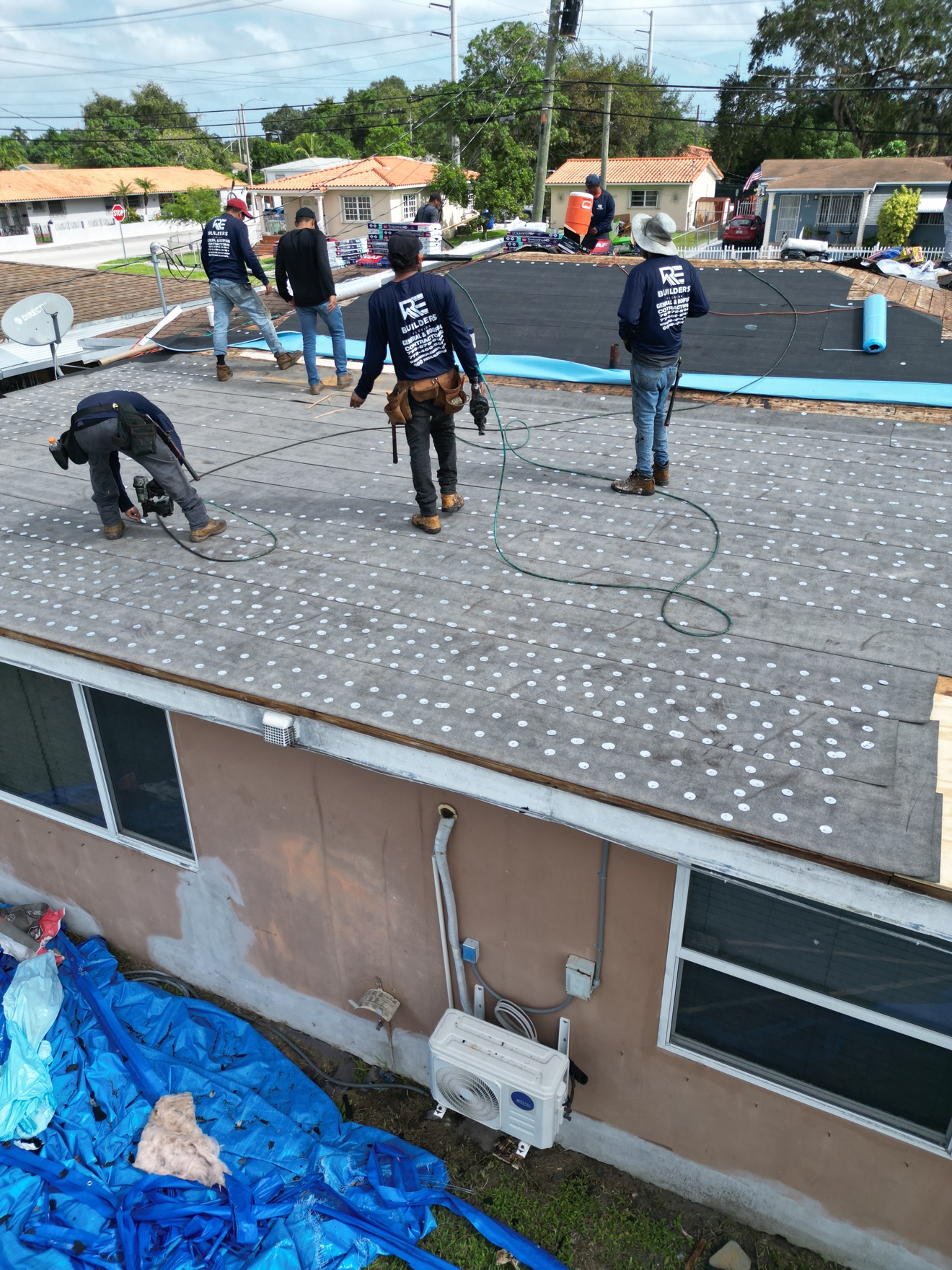 RE Builders crew on a shingle roof with flat section and shingle bundles