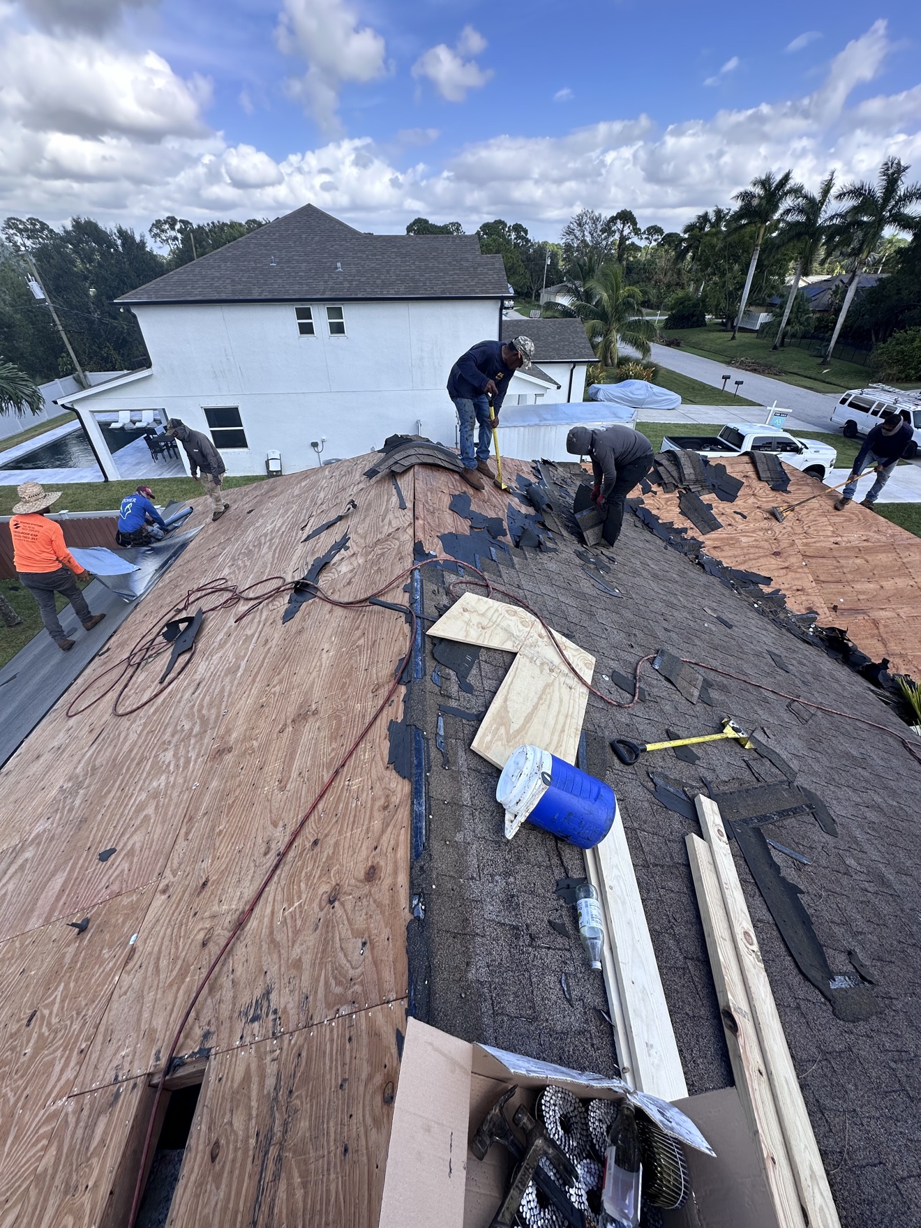 Crew tearing off a shingle roof on a white house with pool