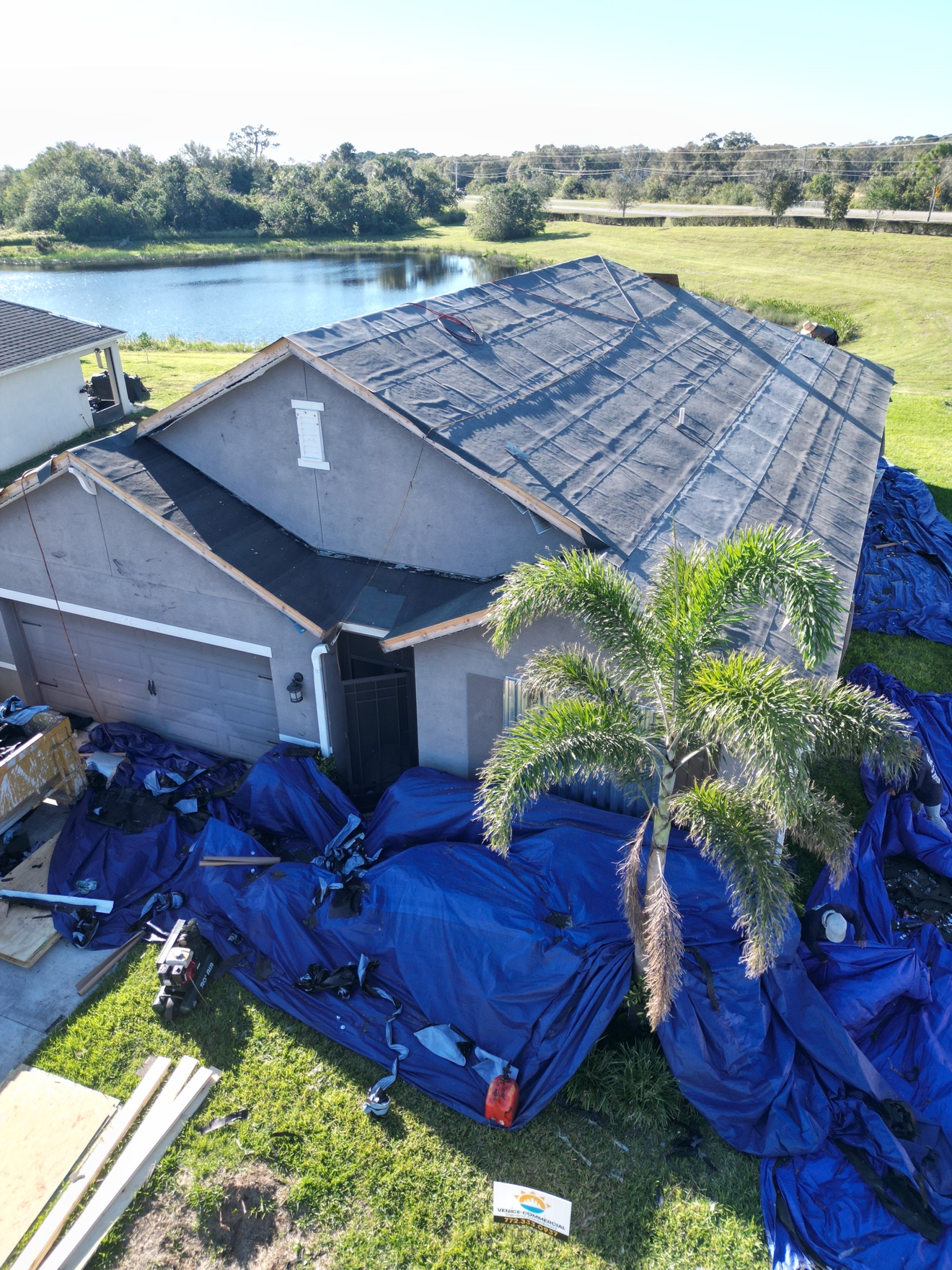 Aerial of a shingle tear-off in progress on a house by a lake